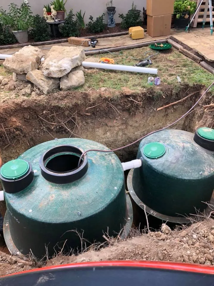 Two green aerobic tanks with open risers set in a fresh excavation