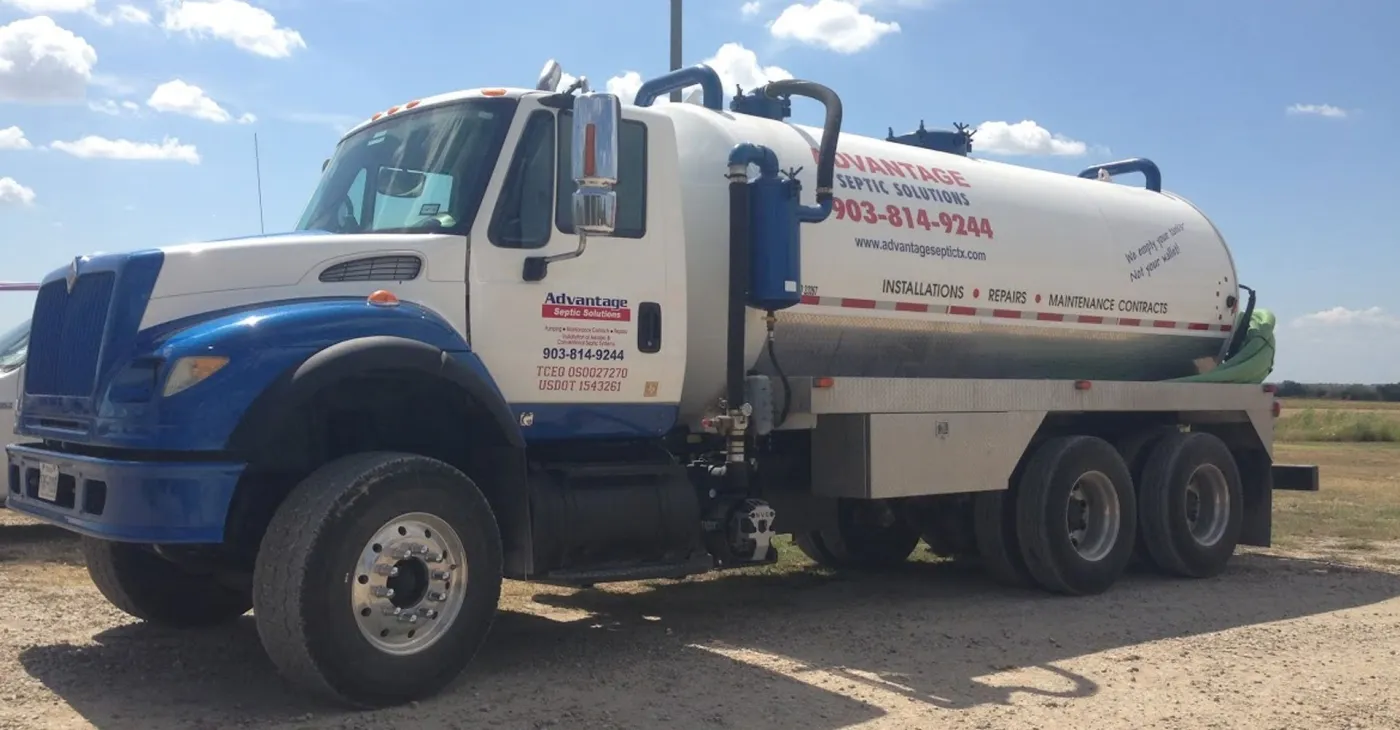 The blue and white Advantage Septic Solutions vacuum pump truck parked on gravel