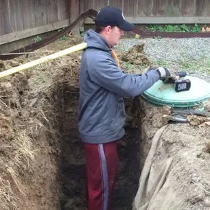 A technician fitting a green riser and lid on a septic tank